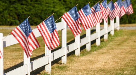 Patriotic display of American flags waving on white picket fence. Typical small town Americana Fourth of July Independence Day decorations.