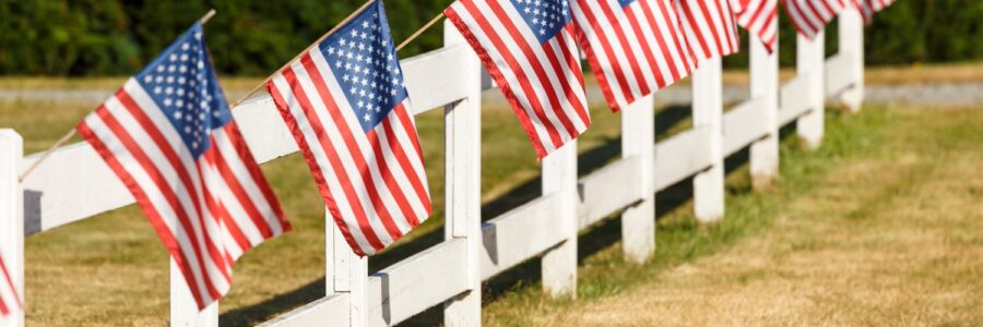 Patriotic display of American flags waving on white picket fence. Typical small town Americana Fourth of July Independence Day decorations.